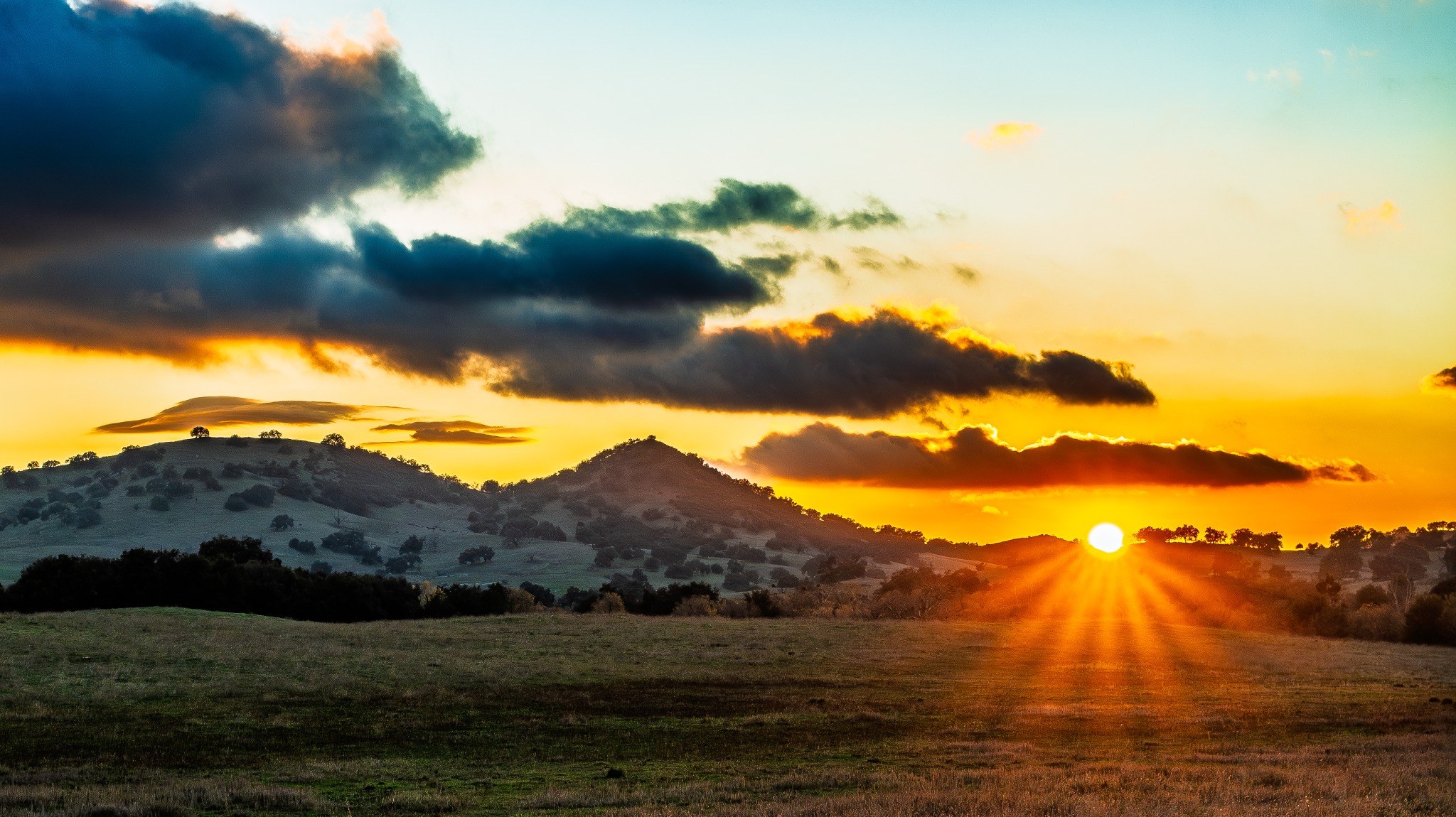 Sunset over rolling hills with rays of golden light